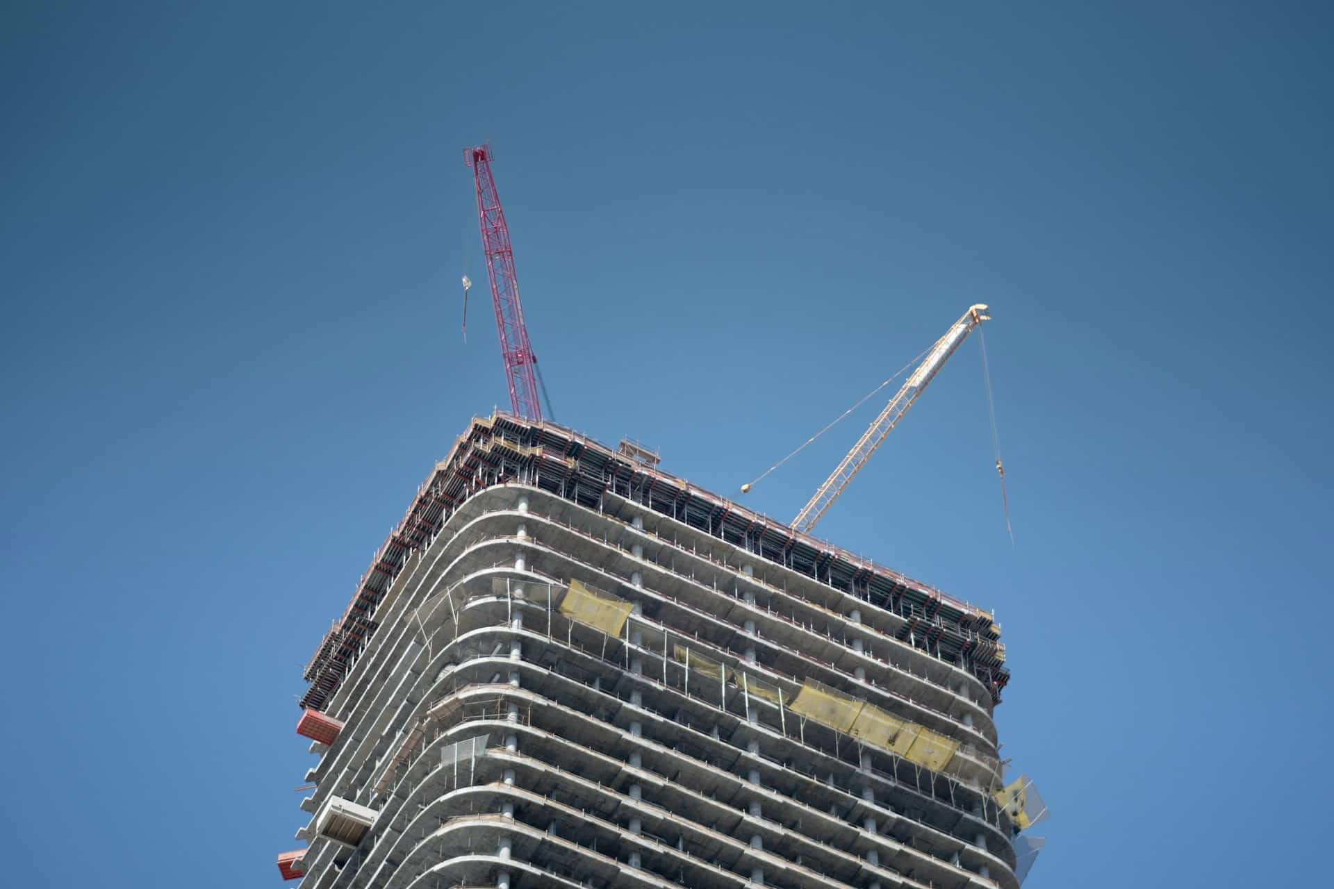 A high-rise building in development with cranes on the top.